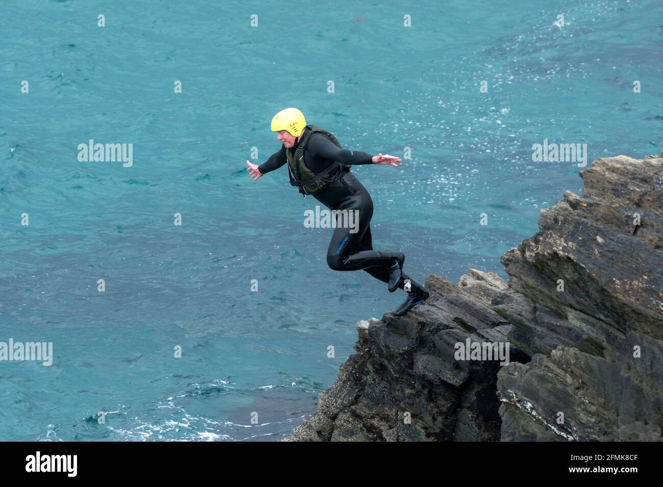 Ein Urlauber, der von den Felsen ins Meer springt, auf einer Fahrt um Towan Head in Newquay in Cornwall. Stockfoto