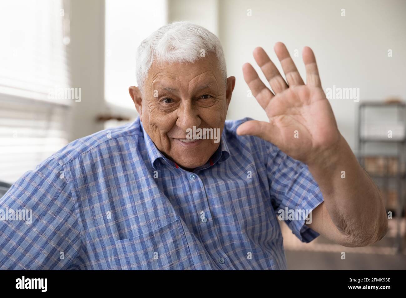 Glücklich lächelnder älterer Mann, der die Kamera anschaut, die Hand hallo winkt Stockfoto