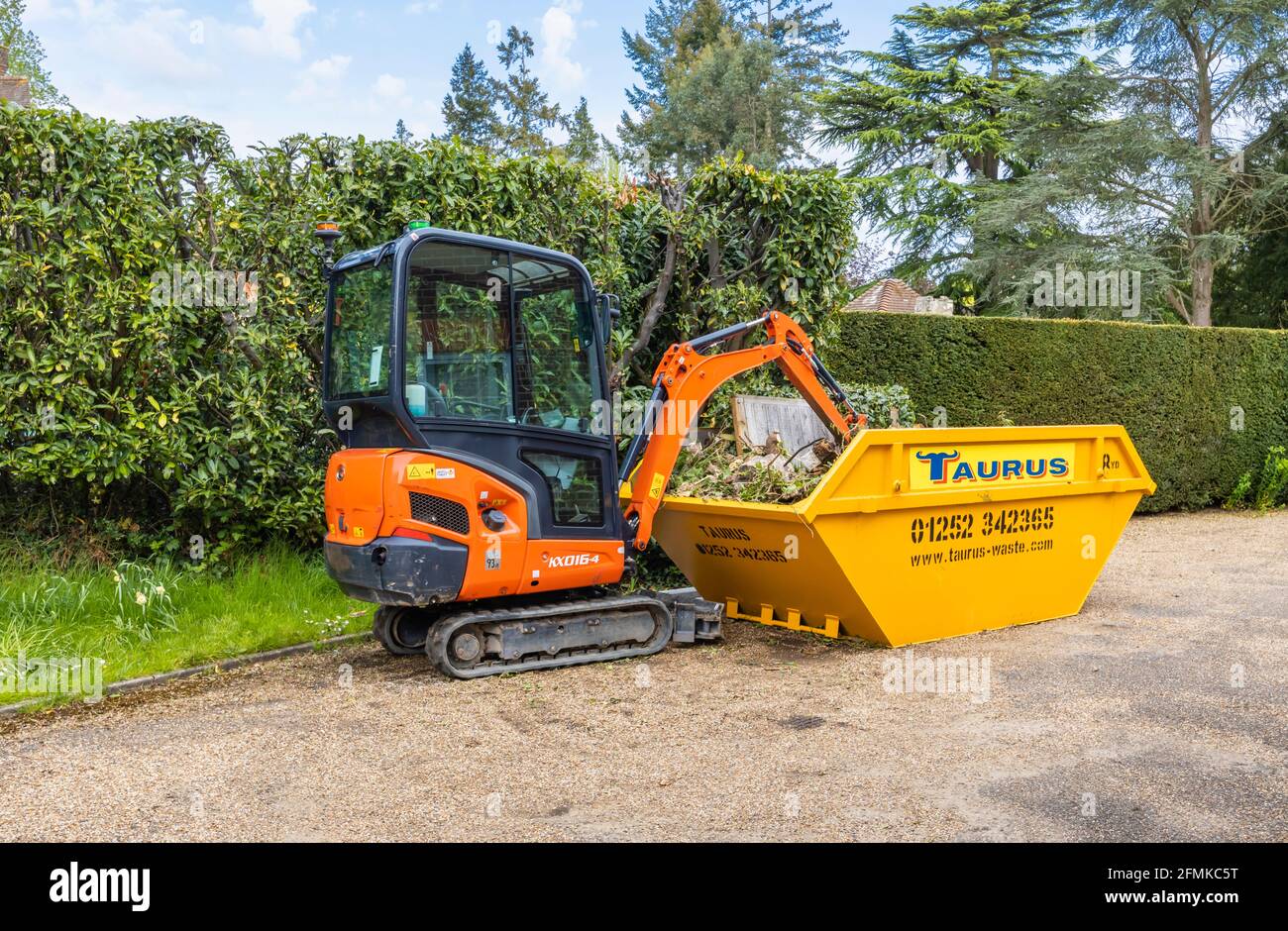Ein Gummifahrzeug mit Raupen, ein orangefarbener Minibagger Kubota KX016-4 und ein gelber überlauf, der für die Gartenreinigung und die Beseitigung von Schutt verwendet wird, Surrey, England Stockfoto