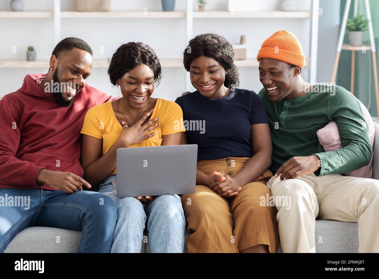 Glückliche schwarze Freunde junge Männer und Frauen mit Laptop, sitzen auf dem Sofa im Wohnzimmer, sehen Film oder Video online, afroamerikanische Paare mit Stockfoto