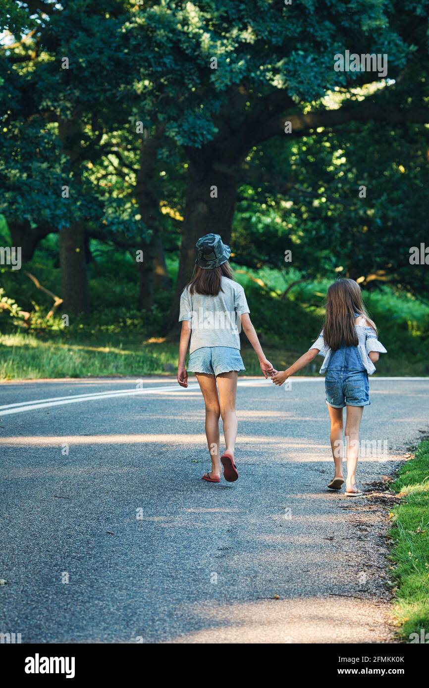 Seltene Ansicht von zwei jungen Mädchen, die Hand in Hand im Park im Freien gehen, London, Großbritannien Stockfoto