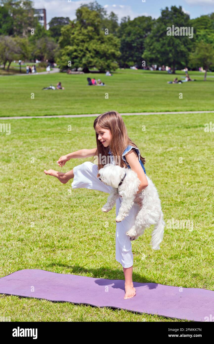 Mädchen mit Hund tut Yoga-Übungen in der Natur im Freien auf Grünes Gras auf der Fitnessmatte, Primerose Hill Park, London, Großbritannien Stockfoto