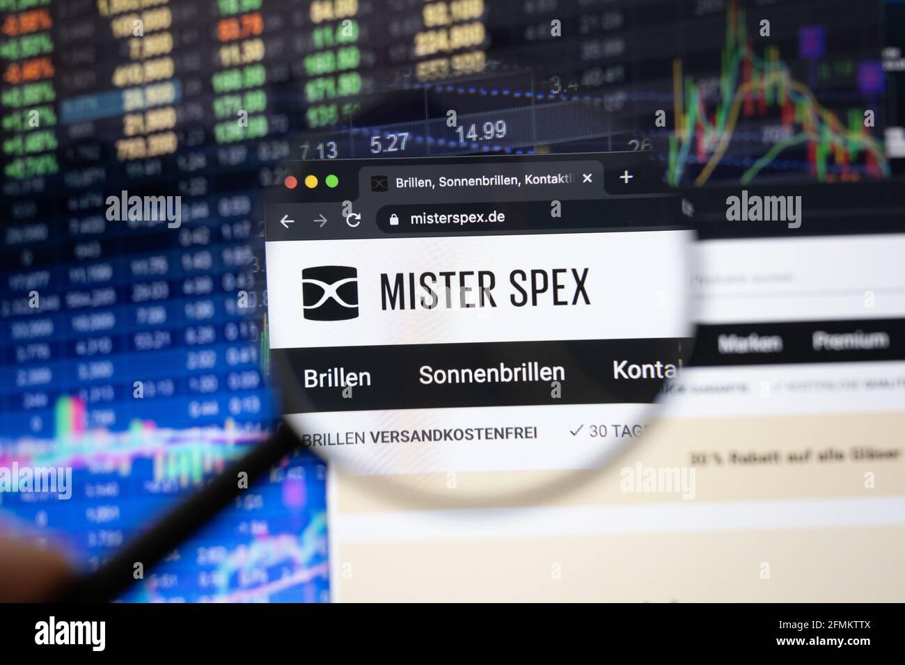 Firmenlogo von Mister Spex auf einer Website mit verschwommenen Börsenentwicklungen im Hintergrund, die auf einem Computerbildschirm durch eine Lupe gesehen werden Stockfoto