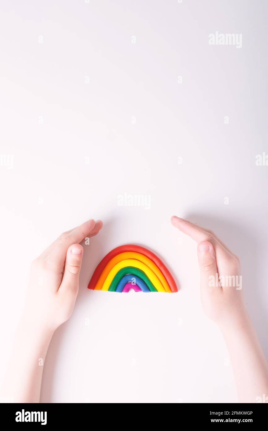 Kinderhände um Plastilin Regenbogen. Konzept der LGBT-Familie. Draufsicht. Farben der Homosexuell Flagge. Heller Hintergrund. Platz oben kopieren. Stockfoto