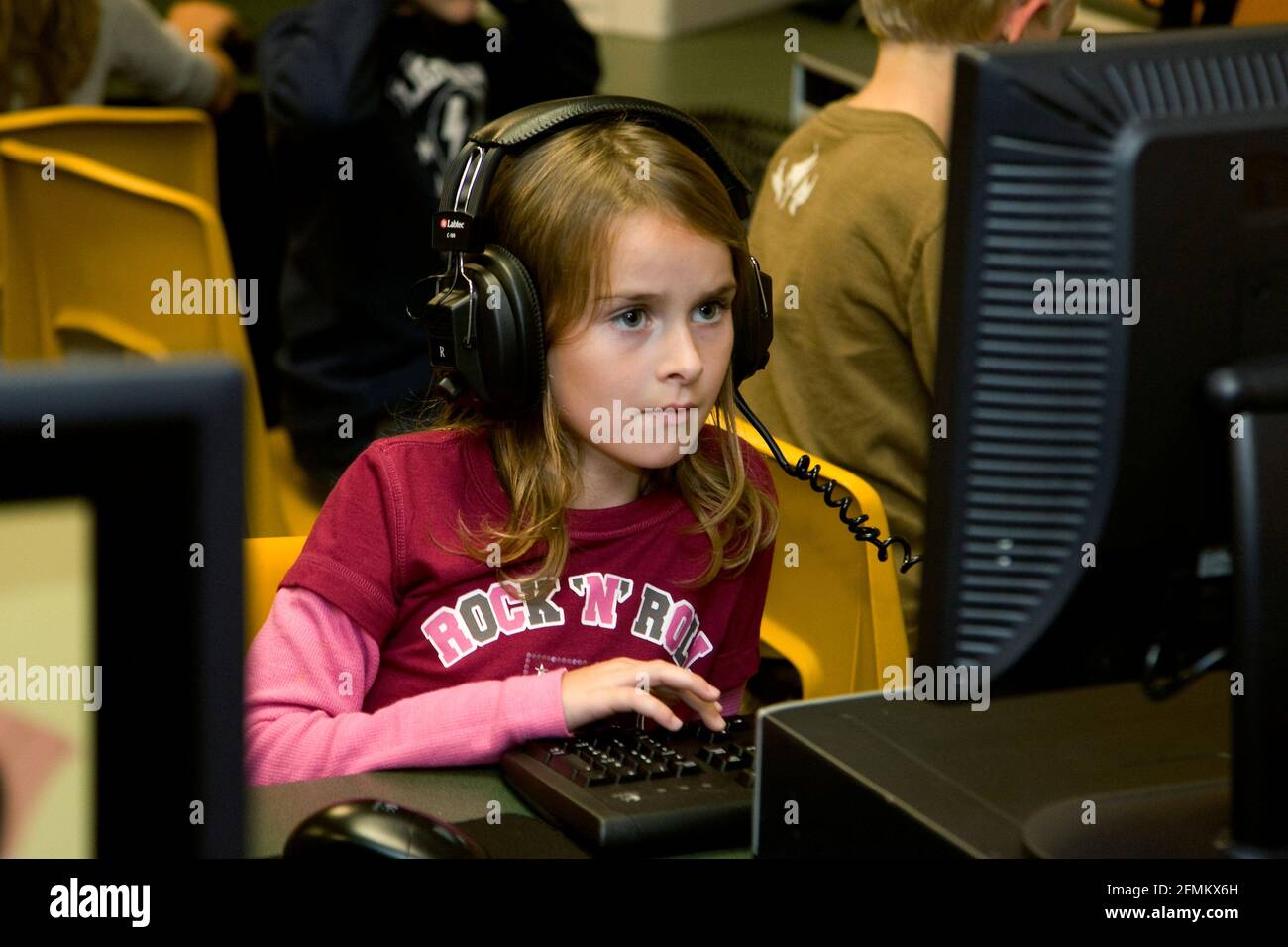 Das Mädchen der Grundschule mit Kopfhörern blickt aufmerksam auf den kompakten Monitor Stockfoto