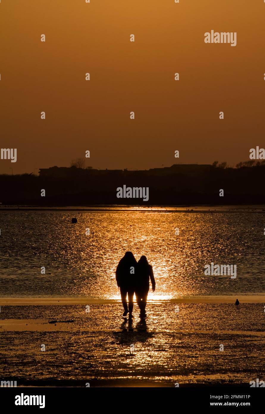 Zwei Personen, ein Paar, das über den Beach Holding läuft, gehen bei Sonnenuntergang mit Reflections in the Water in die untergehenden Sonne, Mudeford Quay UK Stockfoto