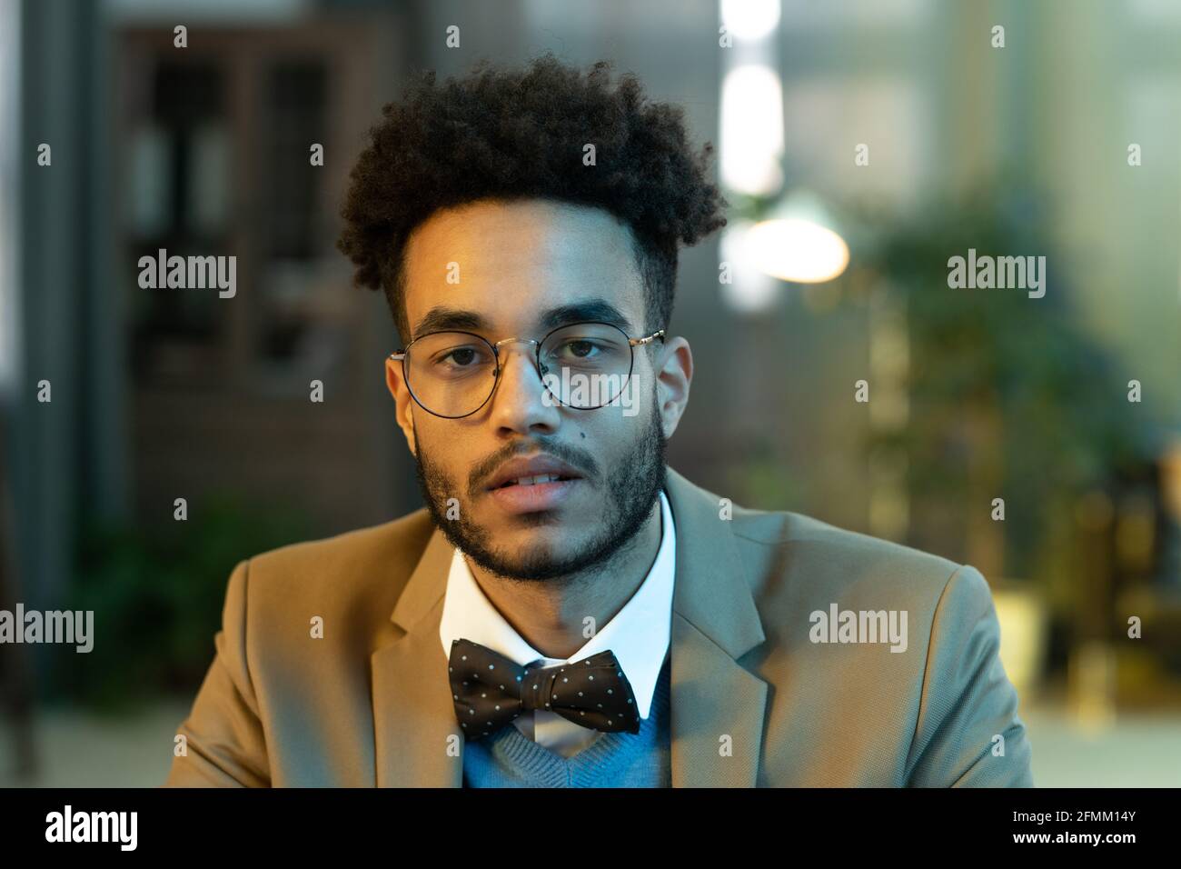 Porträt eines hübschen jungen Mannes mit afro lockigen Haaren Runde Gläser und Fliege sitzen im Büro Stockfoto