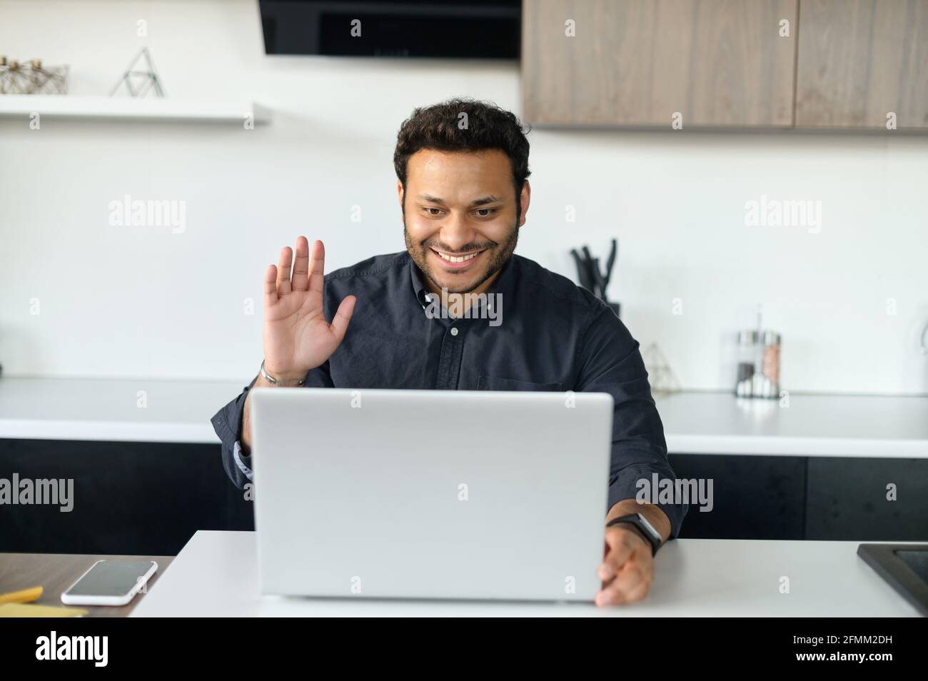 Virtuelle Konferenz. Glücklicher gemischter Kerl mit Laptop für Videoverbindung, multiethnischer Mann begrüßt Online-Gesprächspartner, indischer männlicher Student nimmt Online-Kurse winkt in Webcam, hat Videoanruf Stockfoto