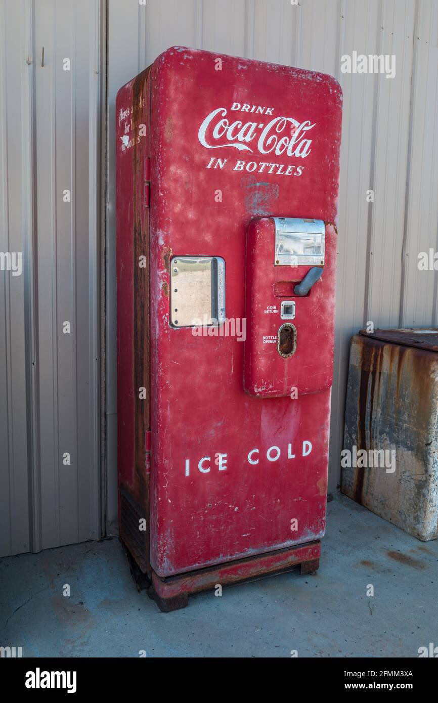 Ein leuchtend roter Coca-Cola-Verkaufsautomat, der mit Original intakt ist Teile und einige Patina stehen senkrecht im Freien gegen ein Gebäude Stockfoto