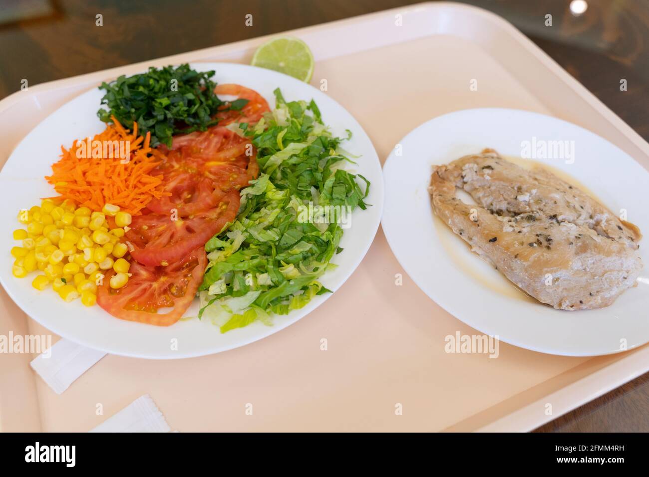 Tablett mit Werksmenüs mit Salat aus Salat, Tomaten, Mais, Karotten und Hühnersteak. Konzept der Mittagspause Stockfoto