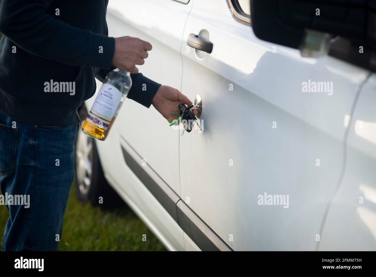 Betrunken in der Leitung eines Wohnmobils Wohnmobil. Ein Mann entriegelt seine Van-Tür mit einer Flasche Whisky-Alkohol in der Hand. Trinken fahren England Großbritannien Stockfoto