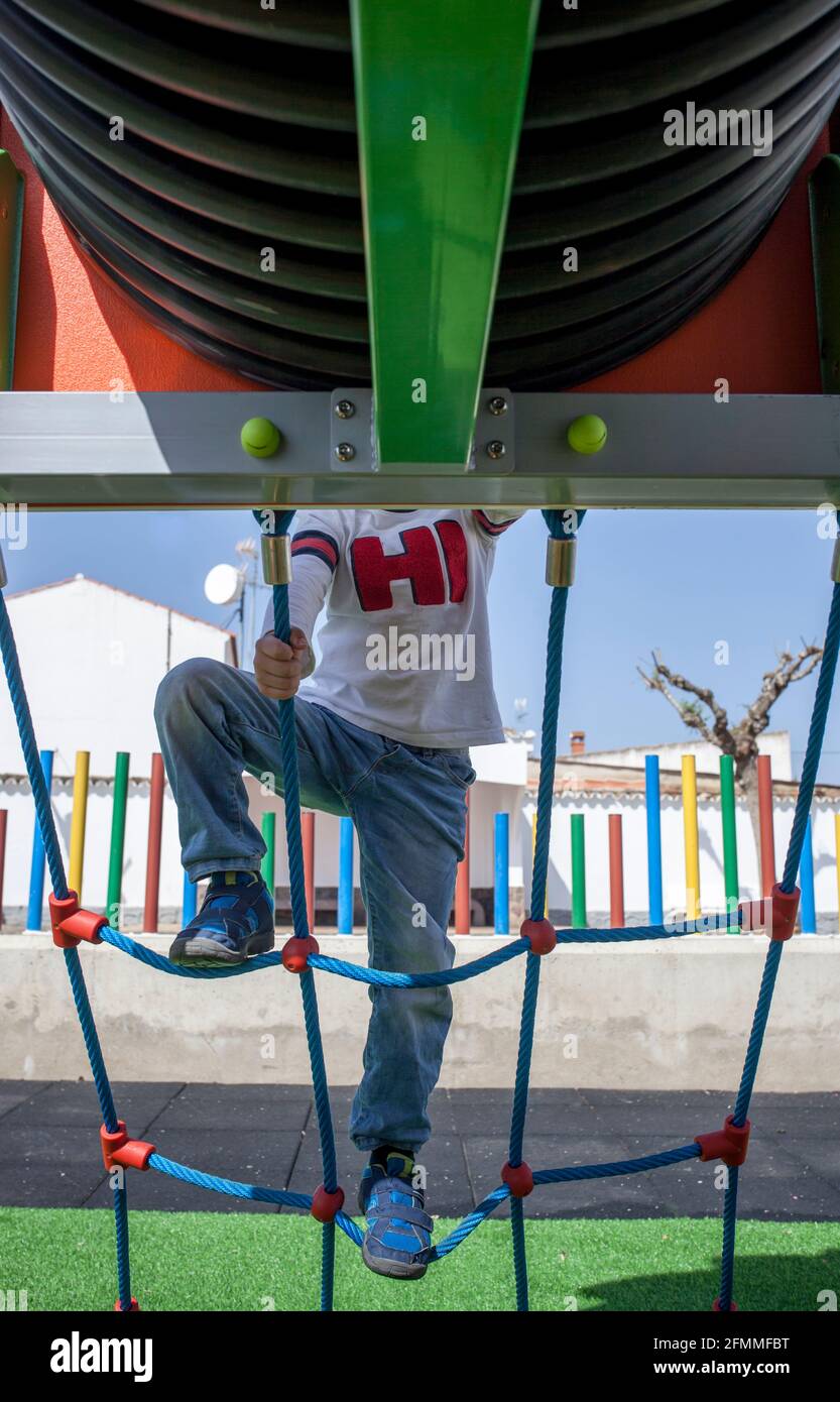 Kind Junge klettert Seilnetz in Richtung des Rohres. Ausrüstung auf einem Spielplatz Stockfoto