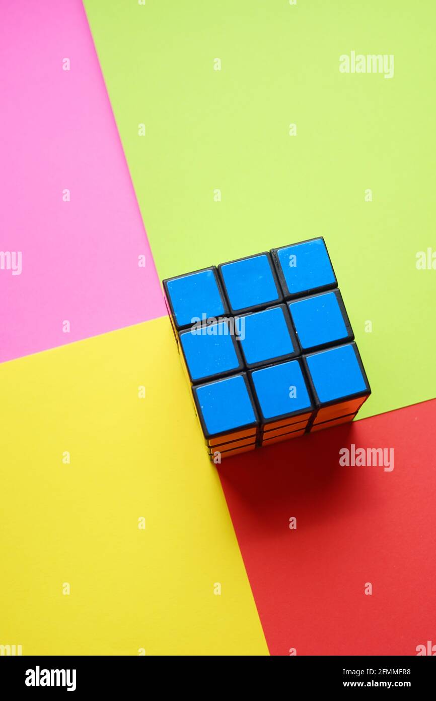 Rubik's würfelblaue Seite auf einem rosafarbenen, rot-gelben Tisch. Stockfoto