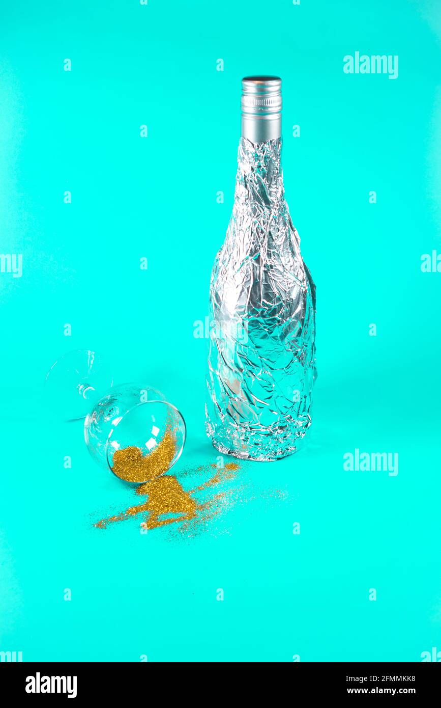 Flasche in Aluminiumfolie und Champagner-Glas mit verschütteten goldenen Glitter eingewickelt. Auf weichem türkisfarbenem Hintergrund. Party- und Sommerkonzept. Stockfoto