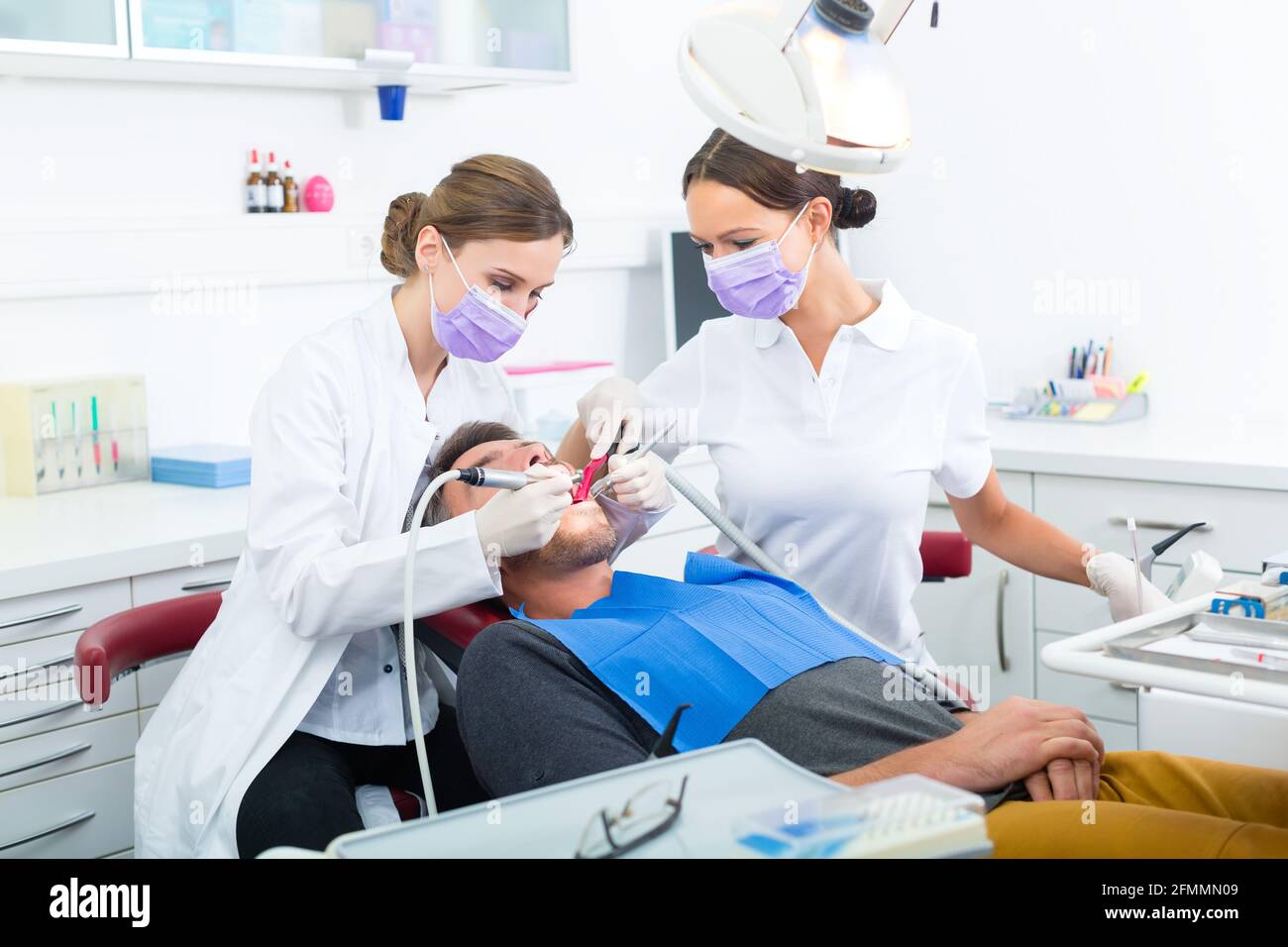 Zahnärztin in ihrer Praxis oder ihrem Büro, die männlichen Patienten mit behandelt Assistent mit Masken und Handschuhen Stockfoto