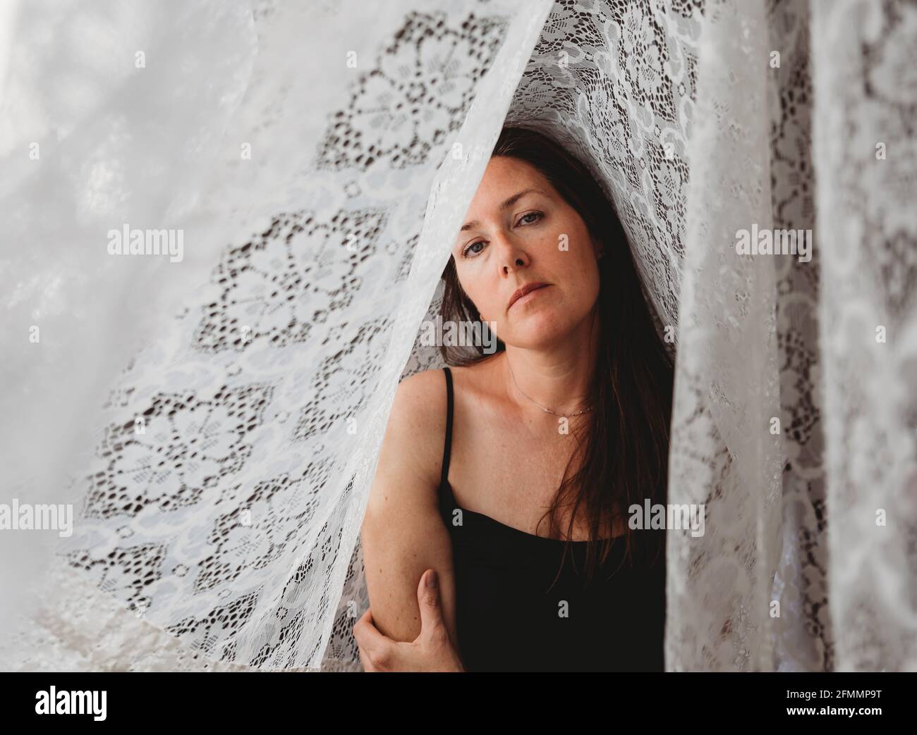 Schöne Frau mit langen braunen Haaren, umgeben von Spitzenvorhängen. Stockfoto