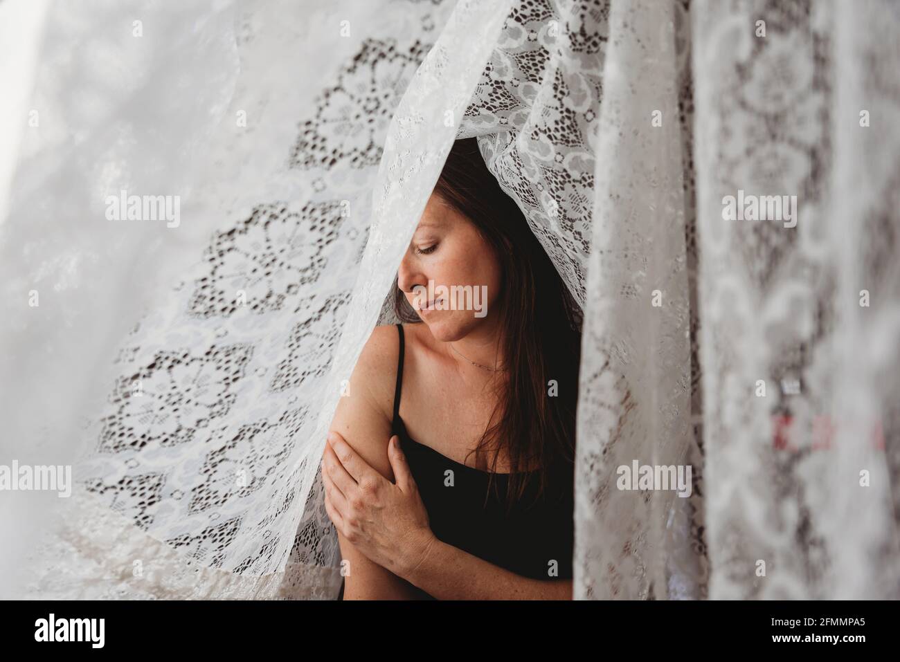 Schöne Frau mit langen braunen Haaren, umgeben von Spitzenvorhängen. Stockfoto