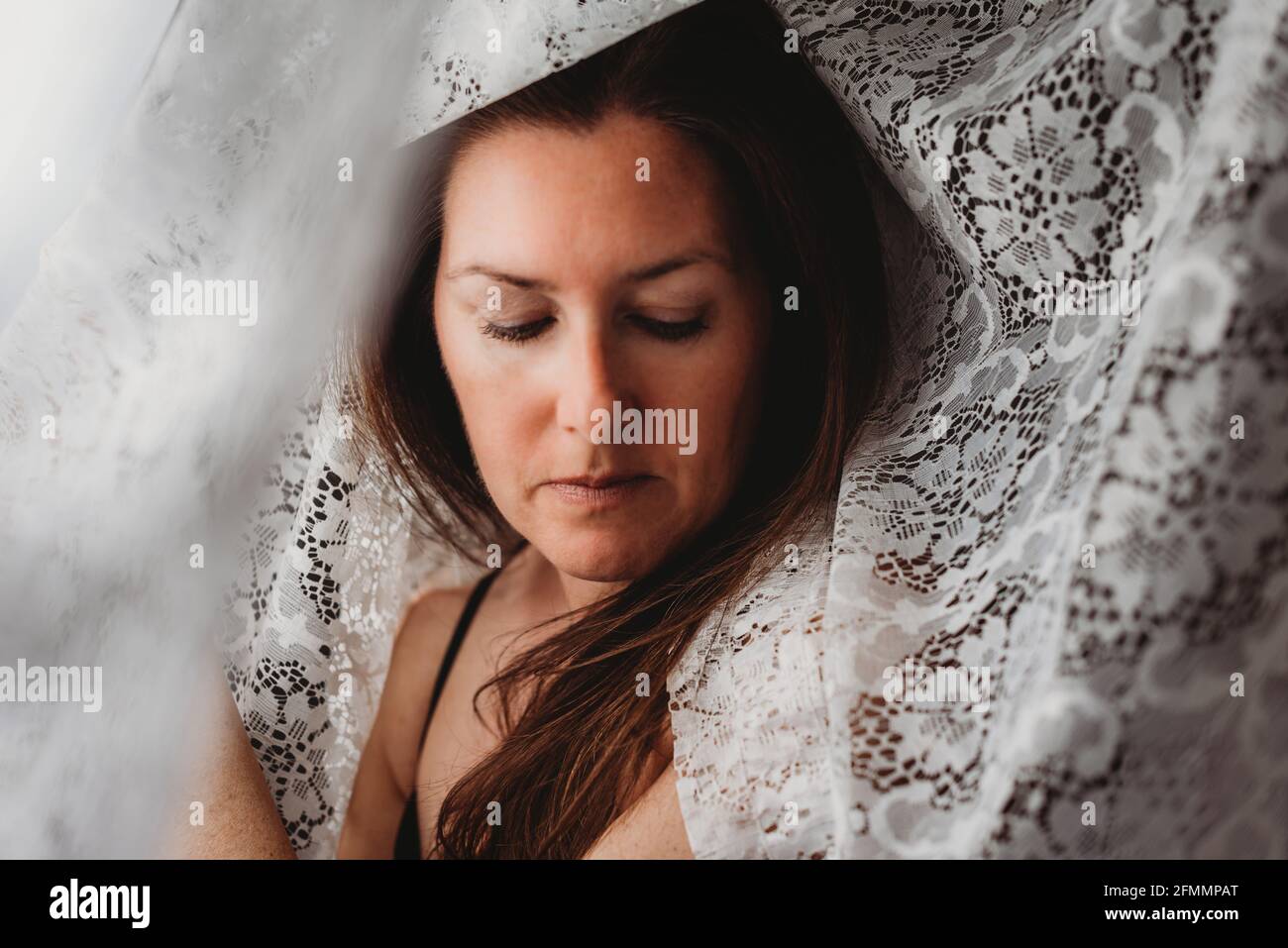 Schöne Frau mit langen braunen Haaren, umgeben von Spitzenvorhängen. Stockfoto