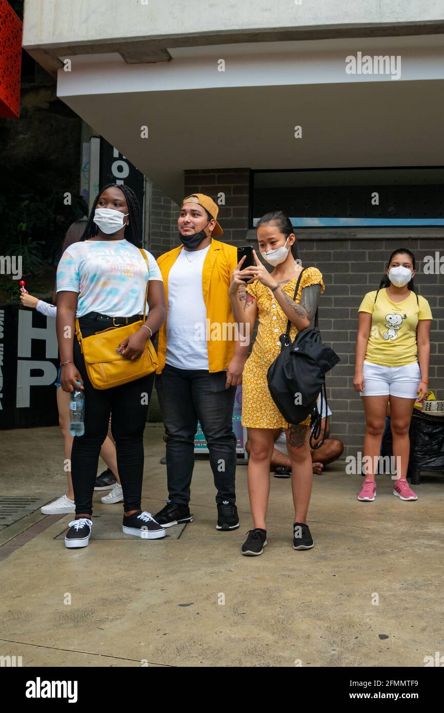 Medellin, Antioquia, Kolumbien - März 27 2021: Junge Afrikanerin mit einem lateinischen Mann und eine asiatische Frau tragen gelbe Kleidung, machen Bilder und Lo Stockfoto