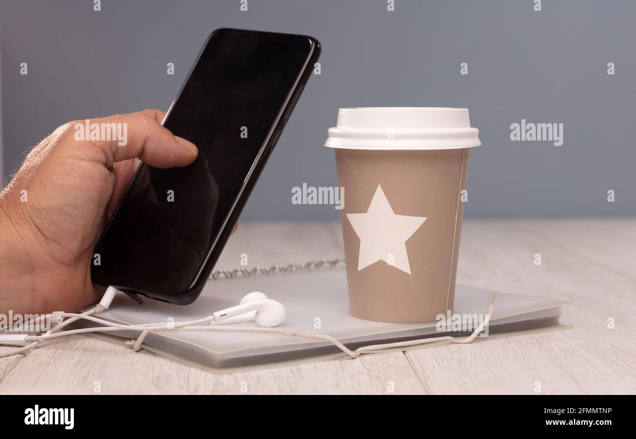 Der Schreibtischmitarbeiter kümmert sich um das Mobiltelefon, ein Glas heißen Kaffees, Kopfhörer und einen Ordner Stockfoto
