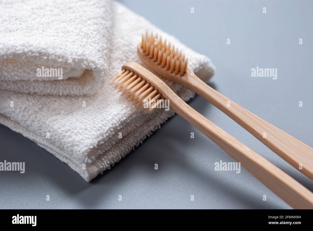 Zwei Zahnbürsten aus Holz und weiße Handtücher auf grauem Hintergrund Stockfoto
