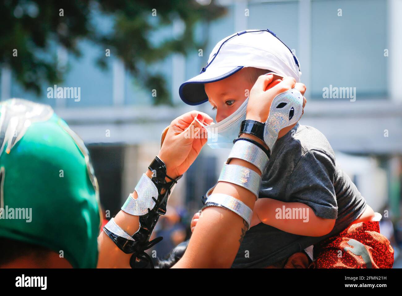 Mexiko, Mexiko. Mai 2021. Ein mexikanischer Luchador hilft einem Kind, eine Gesichtsmaske zu tragen. Die vom mexikanischen Jugendinstitut der Stadt benannte „Brigade zwei von drei Stürzen“ machte eine Runde in der Madero-Straße im historischen Zentrum, um die Verwendung von Gesichtsmasken zu fördern, da die Pandemie trotz der epidemiologischen gelben Ampel immer noch andauert. (Foto von Guillermo Diaz/SOPA Images/Sipa USA) Quelle: SIPA USA/Alamy Live News Stockfoto