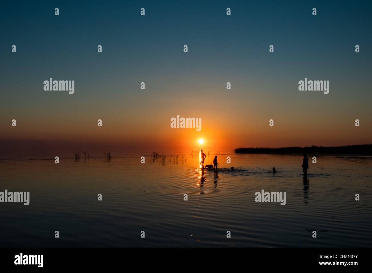 Silhouette einer großen Familie, die bei Sonnenuntergang auf dem See spazierengeht. Konzept des Reisens Familie und genießen Sie die Natur und die Natur. Stockfoto