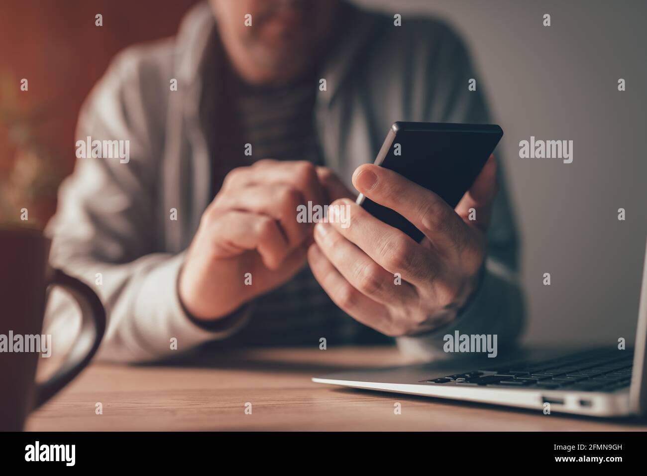 Freiberuflicher Mitarbeiter, der am Schreibtisch des Heimbüros eine SMS auf das Mobiltelefon schreibt, Nahaufnahme mit selektivem Fokus Stockfoto