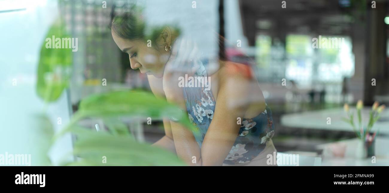 Blick durch die Glaswand der weiblichen Modedesignerin, auf die sie sich konzentriert Ihre Arbeit in der Glaswand Büro Stockfoto