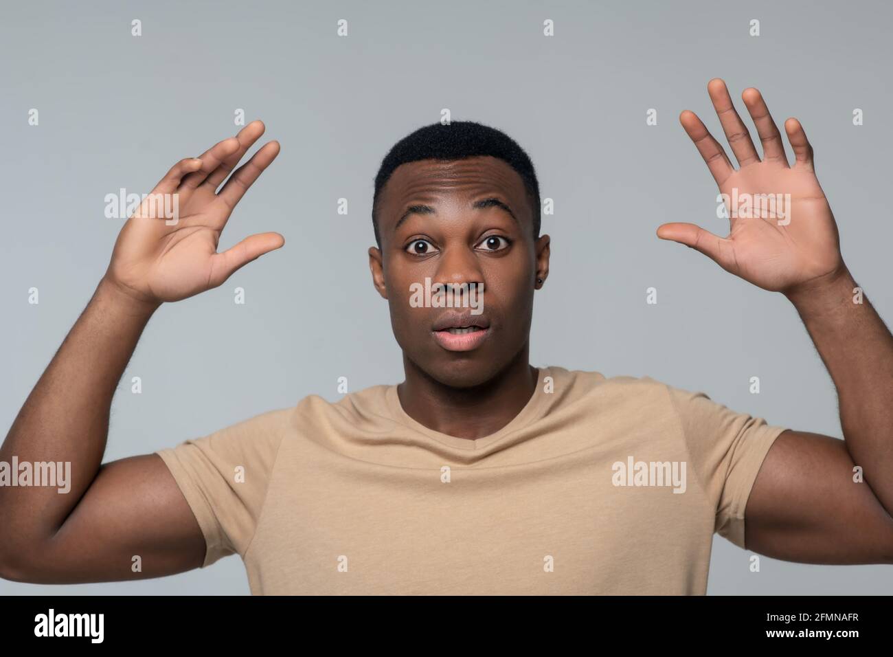 Überrascht junger Mann mit erhobenen Armen gestikuliert Stockfoto