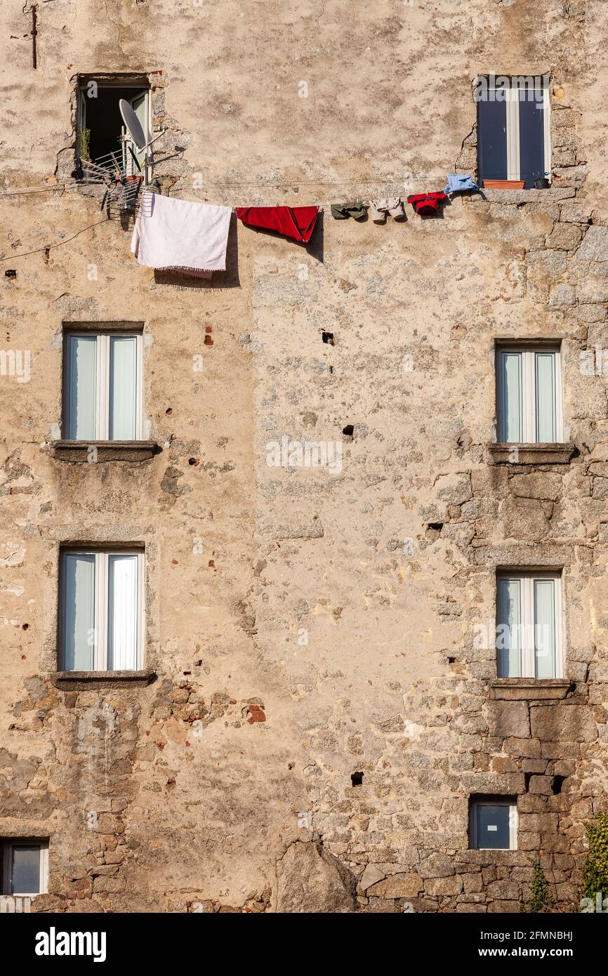 Trocknen der Wäsche zwischen zwei Fenstern der hohen Hausfassade. Sartène, Korsika, Frankreich Stockfoto