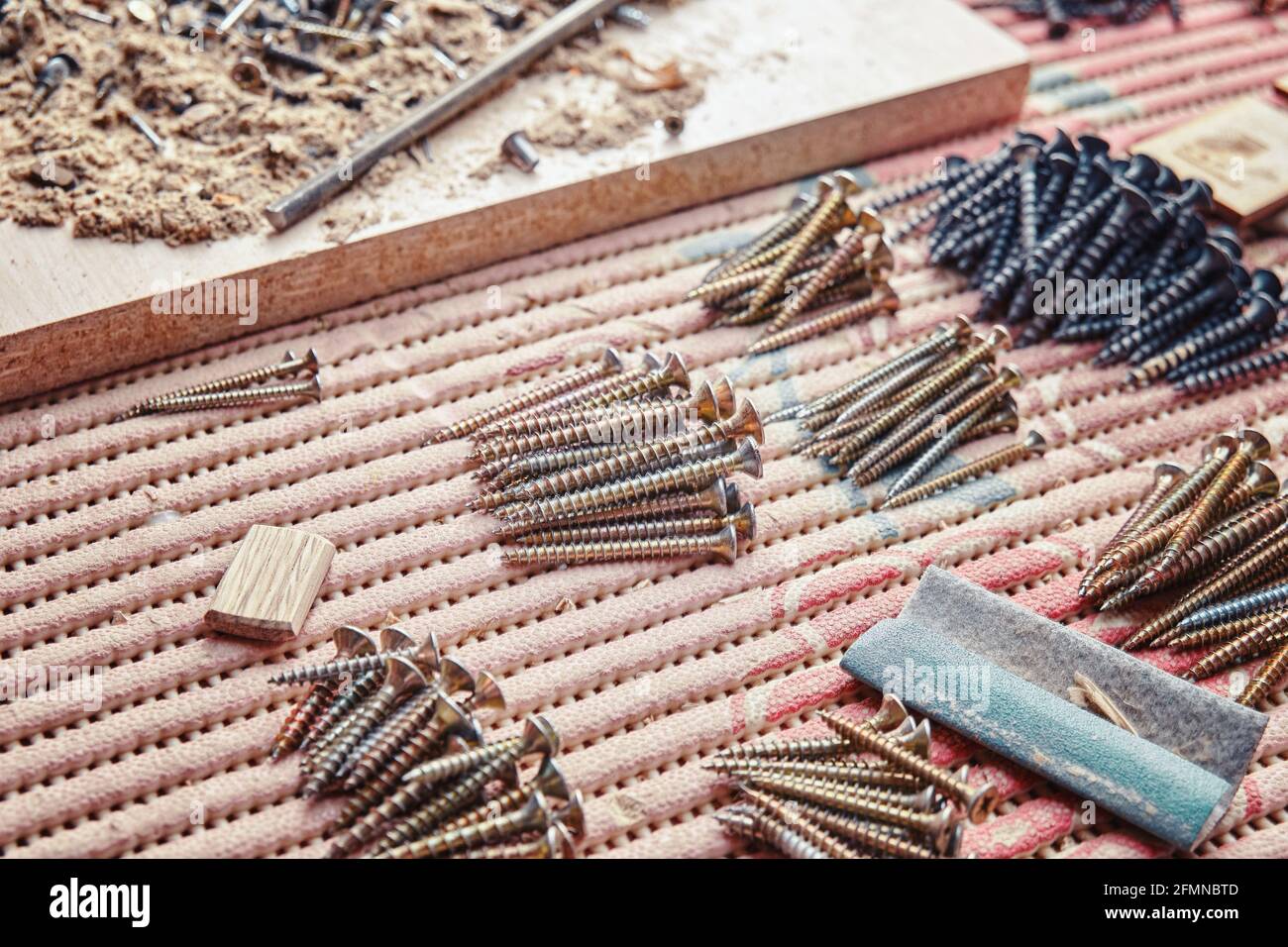 Stapel von modernen selbstschneidenden Schrauben, sortiert nach Größe in der Nähe von Holzarbeiten Reste auf dem Tisch mit farbenfroher Abdeckung extreme Nahsicht Stockfoto