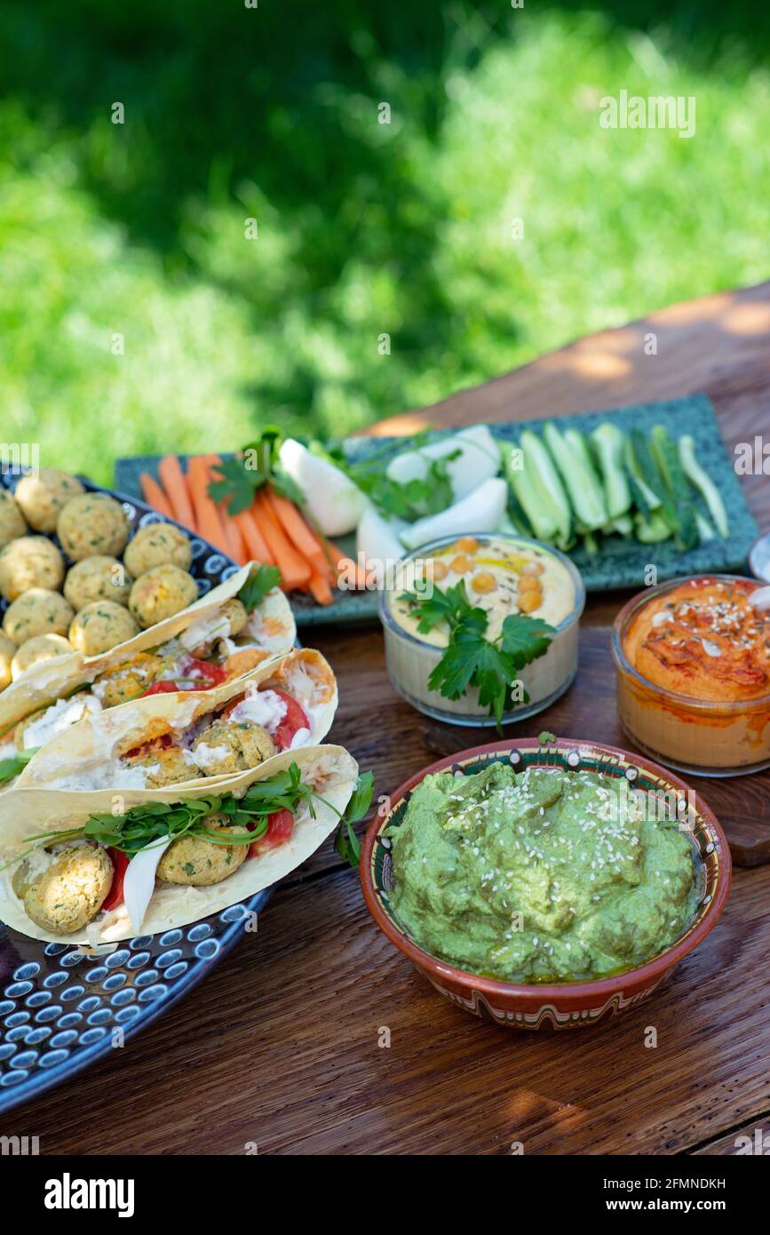 Vegetarisches Picknick auf einem Holzeichentisch, Hummus, Falafel, Pita, Gemüse, Pesto-Sauce aus Spinat, Basilikum und Sonnenblumenkerne. Gesunde mediterrane Küche. Stockfoto