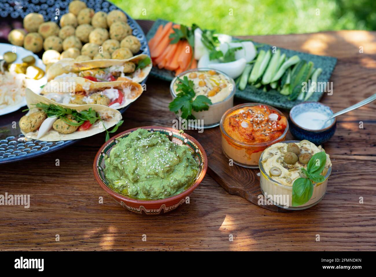 Vegetarisches Picknick auf einem Holzeichentisch, Hummus, Falafel, Pita, Gemüse, Pesto-Sauce aus Spinat, Basilikum und Sonnenblumenkerne. Gesunde mediterrane Küche. Stockfoto