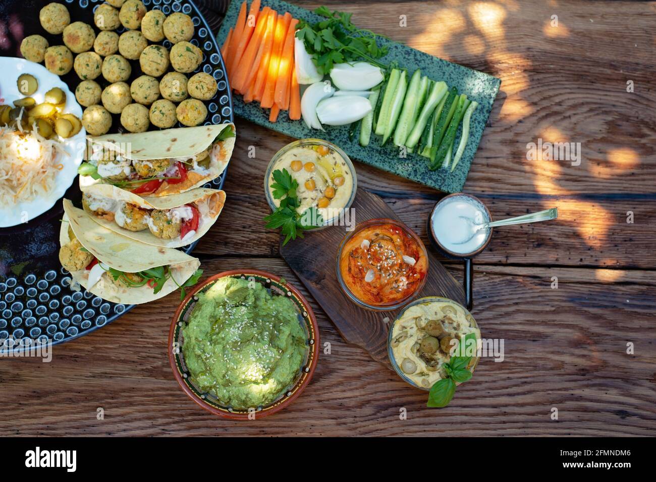 Vegetarisches Picknick auf einem Holzeichentisch, Hummus, Falafel, Pita, Gemüse, Pesto-Sauce aus Spinat, Basilikum und Sonnenblumenkerne. Gesunde mediterrane Küche. Stockfoto