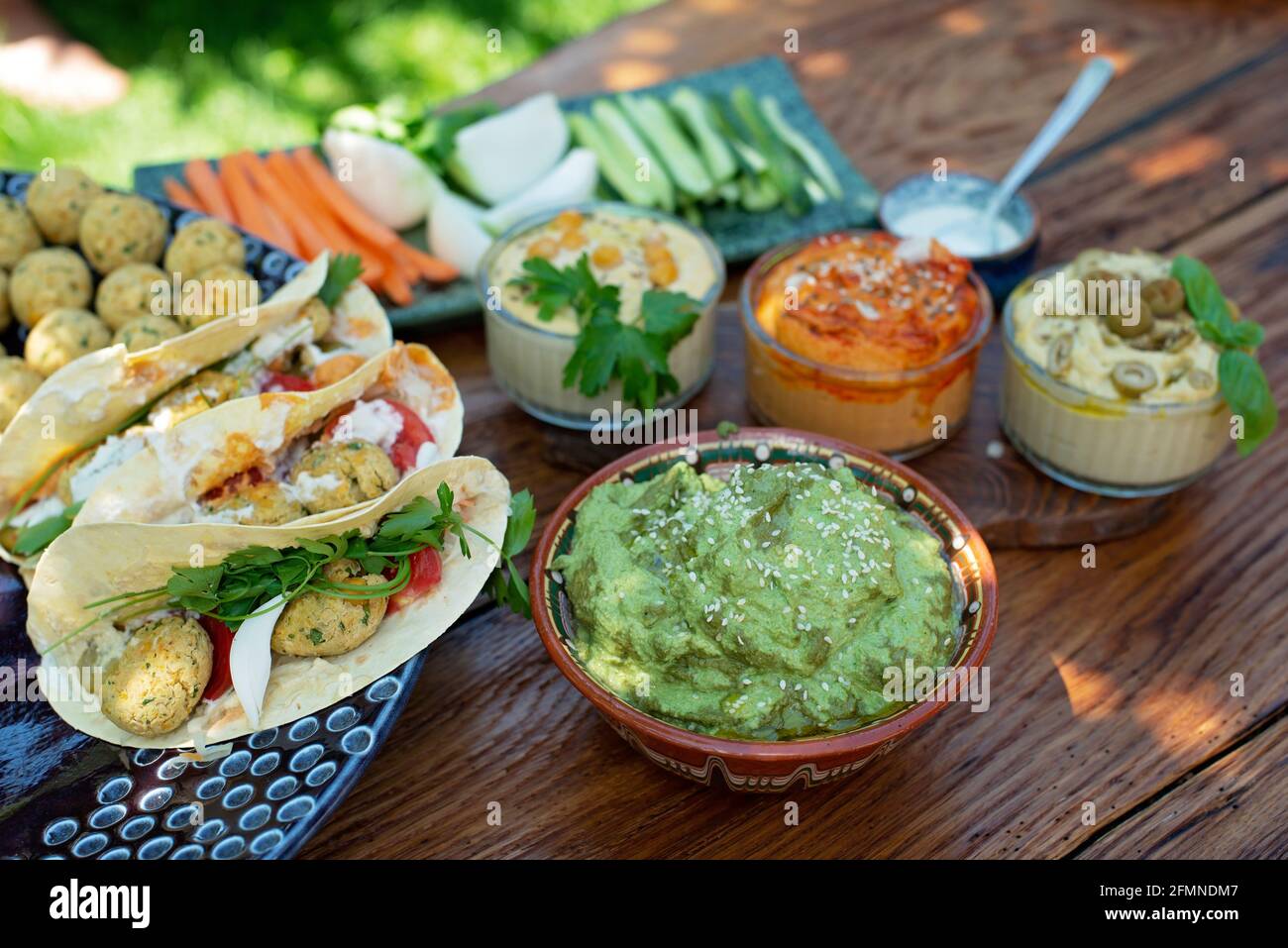 Vegetarisches Picknick auf einem Holzeichentisch, Hummus, Falafel, Pita, Gemüse, Pesto-Sauce aus Spinat, Basilikum und Sonnenblumenkerne. Gesunde mediterrane Küche. Stockfoto