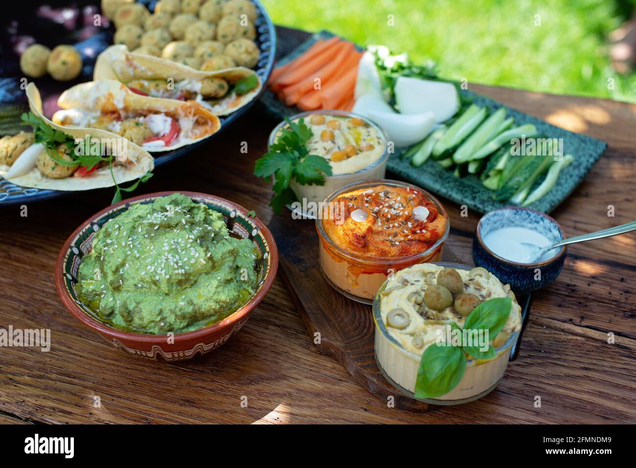 Vegetarisches Picknick auf einem Holzeichentisch, Hummus, Falafel, Pita, Gemüse, Pesto-Sauce aus Spinat, Basilikum und Sonnenblumenkerne. Gesunde mediterrane Küche. Stockfoto