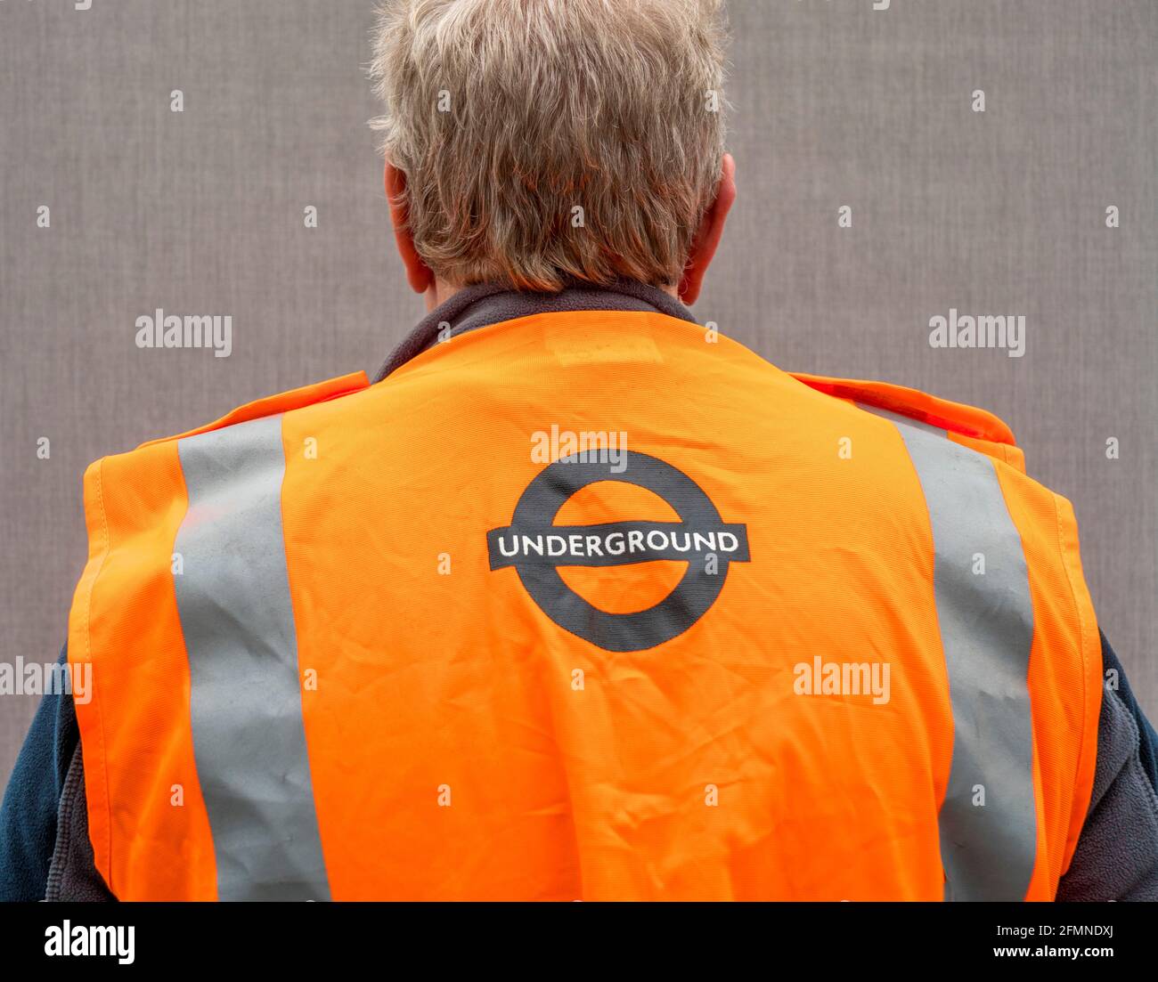 Nahaufnahme des Rückens eines älteren Mannes in Innenräumen, der eine orangefarbene Warnweste der Londoner U-Bahn trägt. Stockfoto