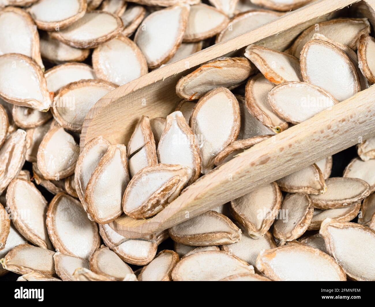 Holzlöffel auf Stapel von ungeschälten Kürbiskernen in Nahaufnahme Stockfoto