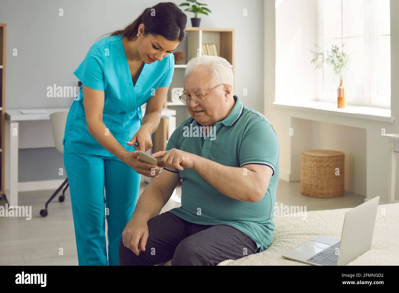 Gesundheitshelferin lehrt ihre ältere Patientin, die Gesundheits-App zu verwenden Auf seinem Mobiltelefon Stockfoto