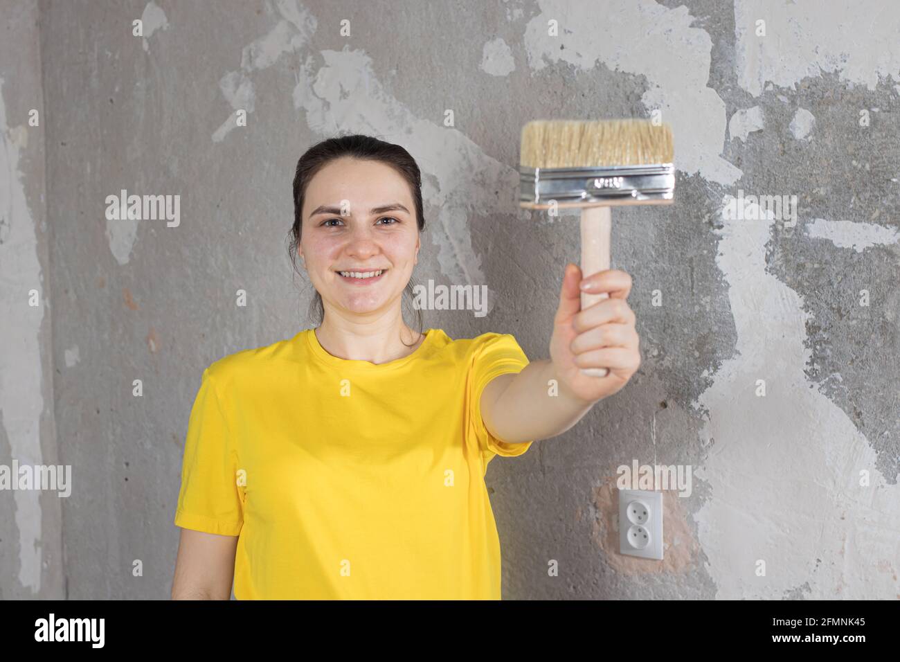 Eine Reparaturfrau in einem gelben, hellen T-Shirt hält einen Pinsel und lächelt. Platz für Text kopieren. Schlüsselfertige Reparaturen Stockfoto