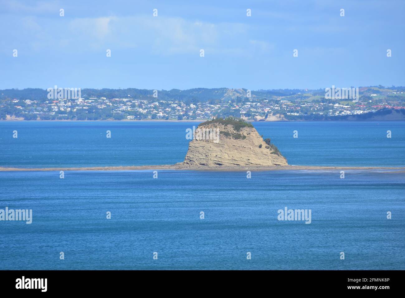 Winzig kleine felsige Insel mit einigen Grasbedeckung auf einem felsigen Riff, das bei Ebbe aus dem blauen Meer ragt. Stockfoto