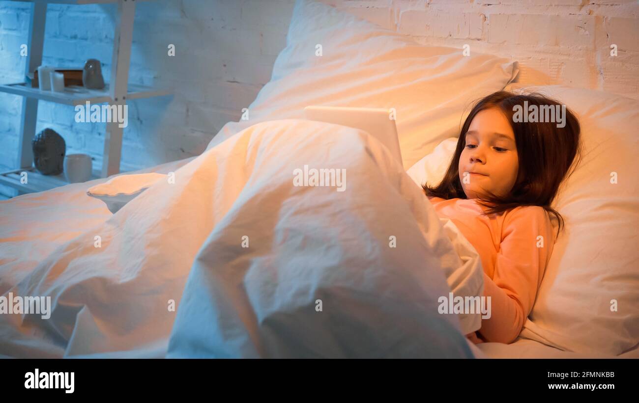 Kind mit digitalem Tablet im Bett Stockfoto