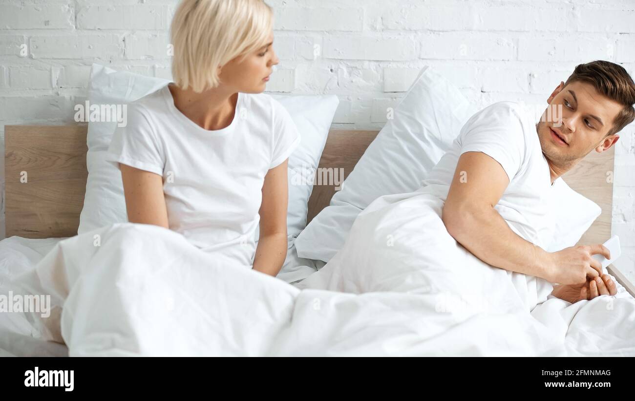 Blonde Frau, die ihren Freund mit dem Smartphone im Schlafzimmer ansieht Stockfoto