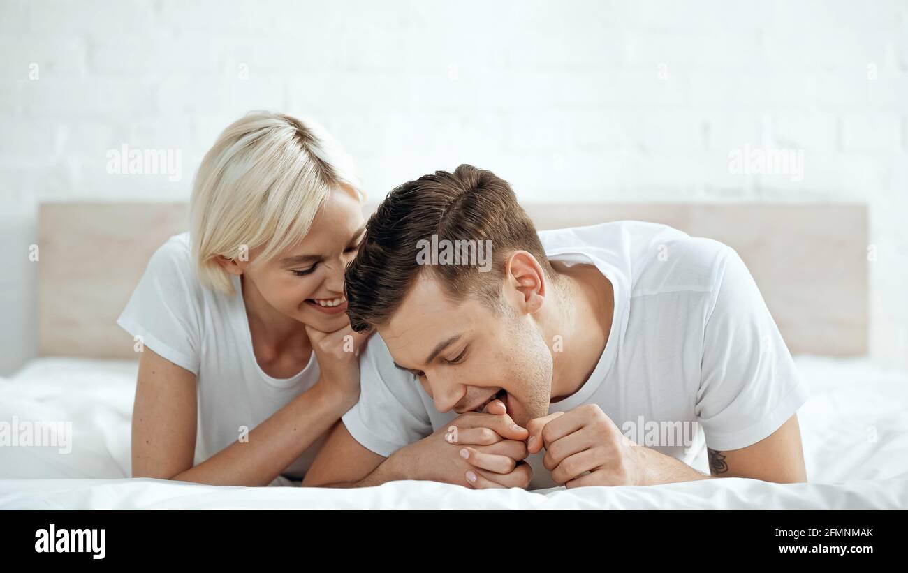 Lustiger Mann beißt die Hand einer fröhlichen Frau auf dem Bett Stockfoto