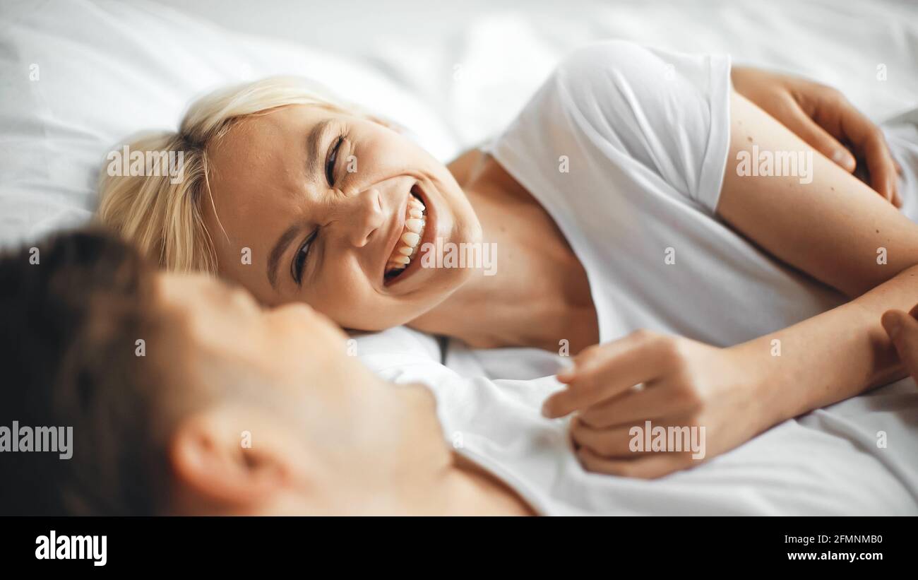 Fröhliche Frau, die lachte, während sie mit ihrem Freund auf dem Bett lag Verschwommener Vordergrund Stockfoto