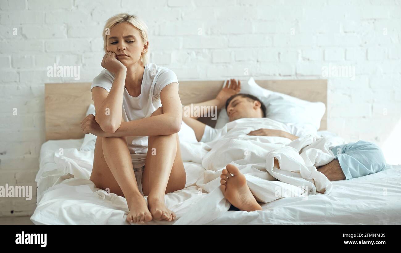 Gelangweilt und barfuß Frau auf dem Bett sitzen, während Freund schlafen Im Schlafzimmer Stockfoto