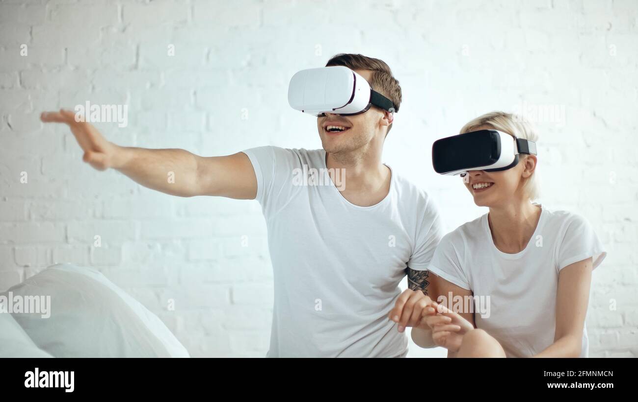 Glücklicher tätowierte Mann und fröhliche blonde Frau in vr Headsets Stockfoto