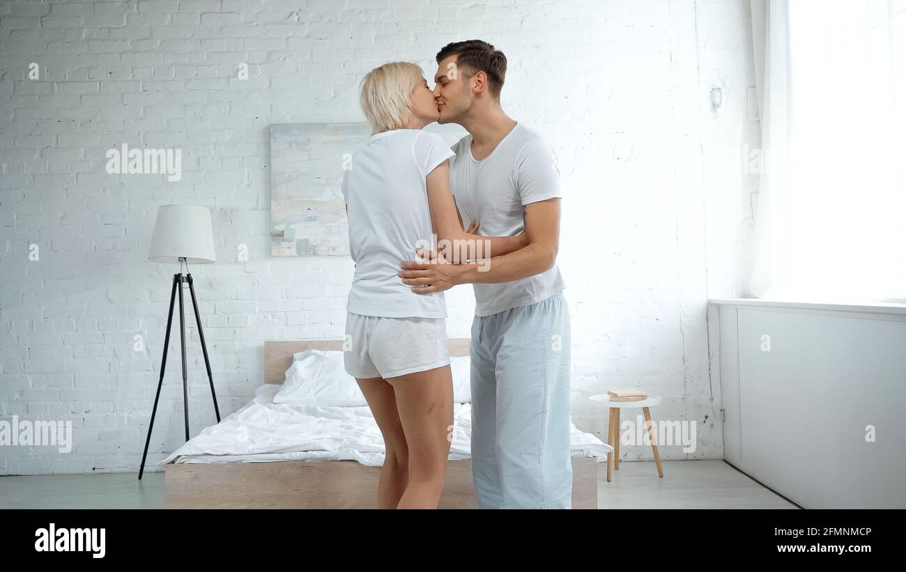Glücklicher Mann umarmt und küsst blonde Frau im Schlafzimmer Stockfoto