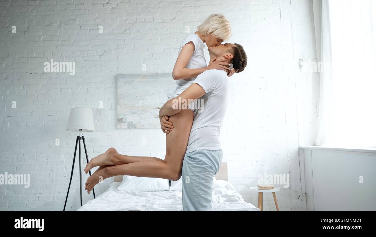 Seitenansicht des Mannes, der in den Armen hält und blonde küsst Frau im Schlafzimmer Stockfoto